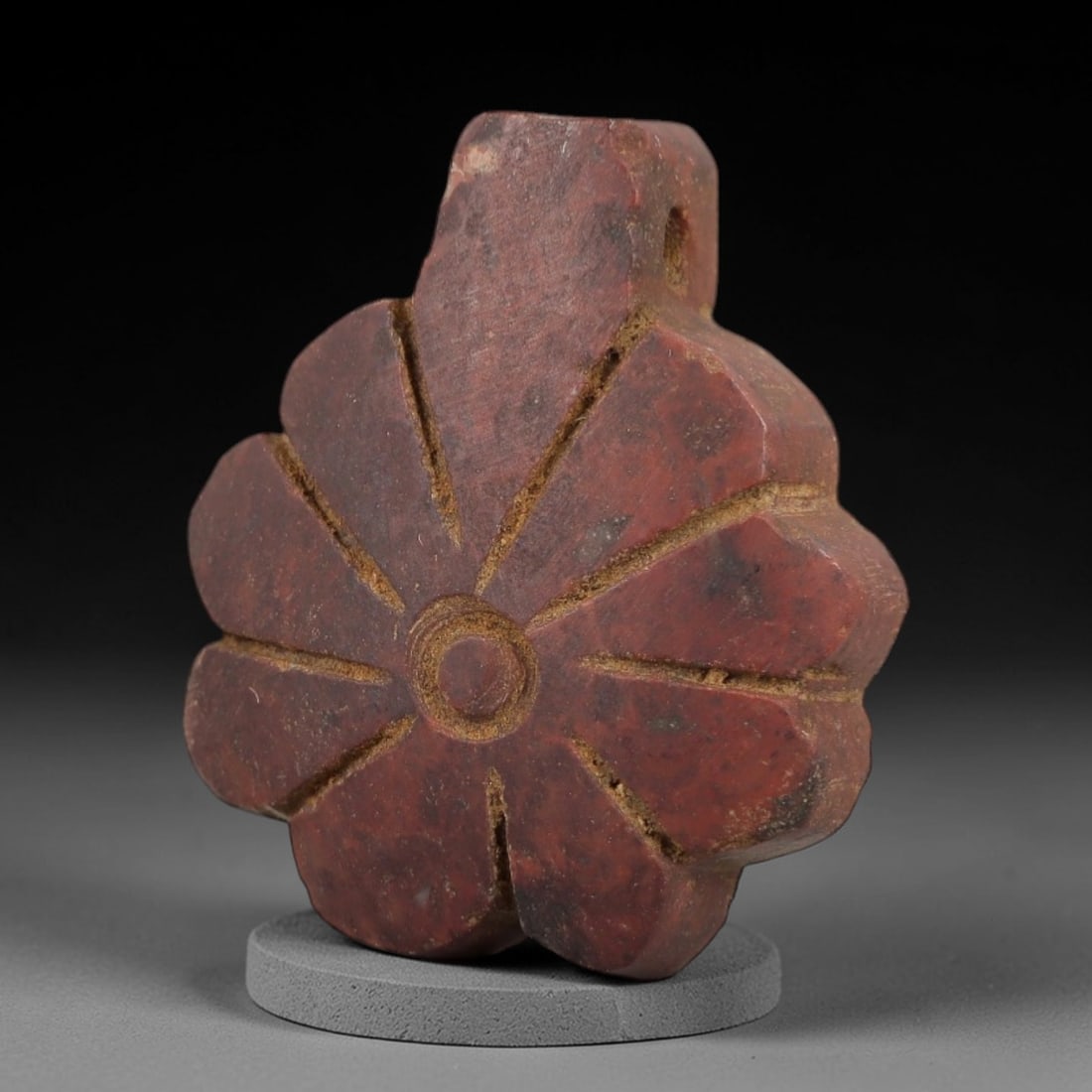Ancient Egyptian Stone Amulet - Carved Ritual Pendant, 12AG: Carved from reddish-brown stone, this amulet features a central circular motif with radiating linear patterns, typical of small Egyptian ritual pendants from the Late Period. The form is designed for