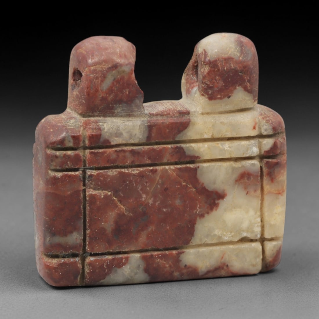 Ancient Stone Amulet - Near Eastern Double Loop Pendant, 64XQ: This amulet is carved from a variegated red-and-white brecciated stone, featuring a rectangular body with two raised, perforated suspension loops at the upper edge, confirming its use as a wearable pr