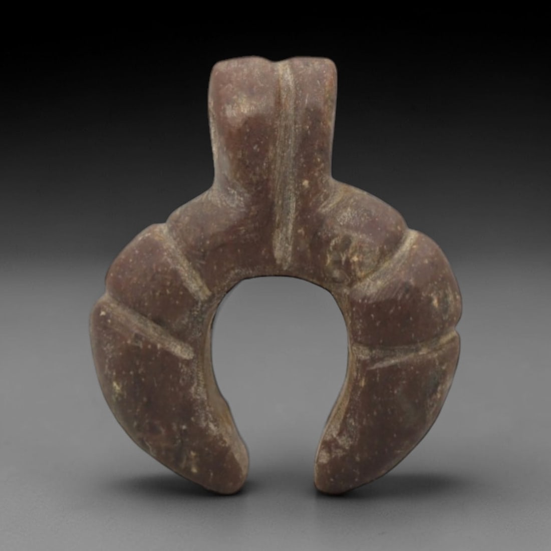 Ancient Stone Amulet - Near Eastern U-Shaped Pendant, 62XQ: This amulet is carved from a dense, reddish-brown stone, shaped into a symmetrical U-form with a raised rectangular suspension loop at the top, confirming its use as a wearable protective charm. The c