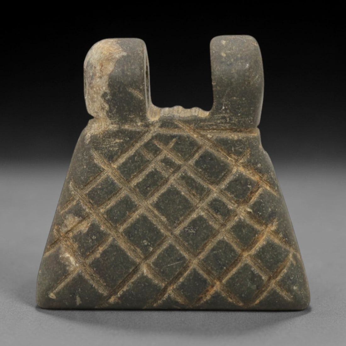 Ancient Stone Amulet - Near Eastern Grid Pattern Pendant, 60XQ: This amulet is carved from a dense, dark gray stone, exhibiting a compact triangular form with two raised, perforated suspension loops at the upper edge, indicating its use as a wearable protective ch
