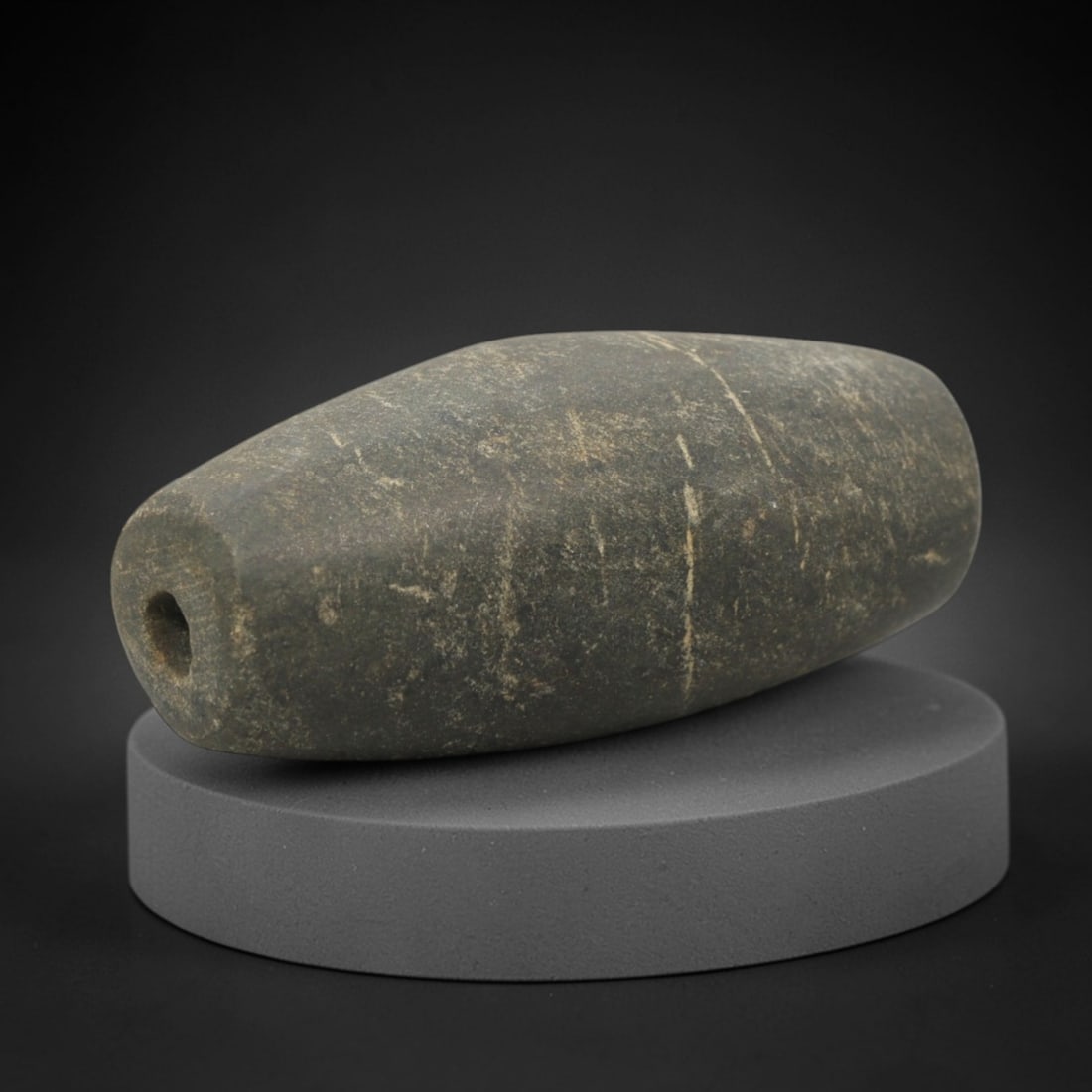 Ancient Stone Bead - Near Eastern Amulet Pendant, 54XQ: Carved from a dense, dark grey stone with natural light veining, this bead takes an elongated, biconical form with a central perforation drilled through its length for stringing. The surface is smooth