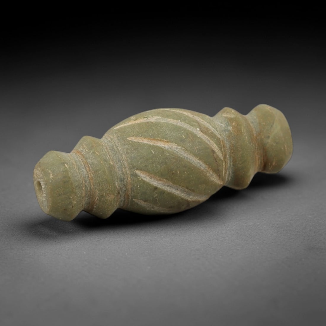 Ancient Egyptian Stone Amulet - Carved Ritual Pendant, 67AE: Carved from greyish-green stone, this amulet features ribbed linear patterns along its elongated form, typical of small Egyptian ritual pendants from the Late Period. The shape is designed for suspens