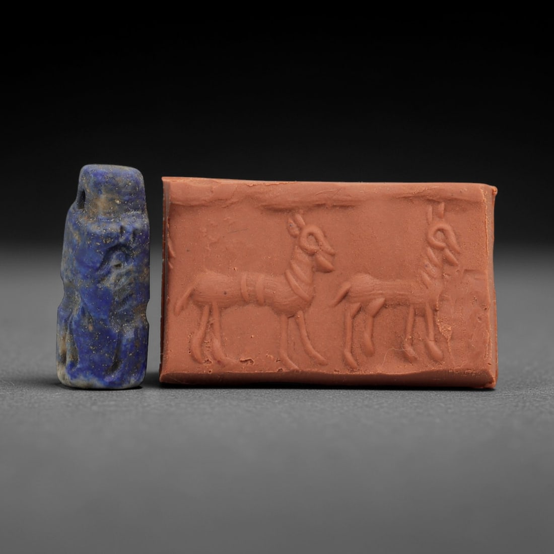 Ancient Near Eastern Lapis Lazuli Cylinder Seal - Stag Motif, 64AH: Carved from lapis lazuli, this small cylinder seal features incised depictions of paired stags, a motif common in ancient Near Eastern glyptic art. The piece exhibits a natural deep blue patina with m