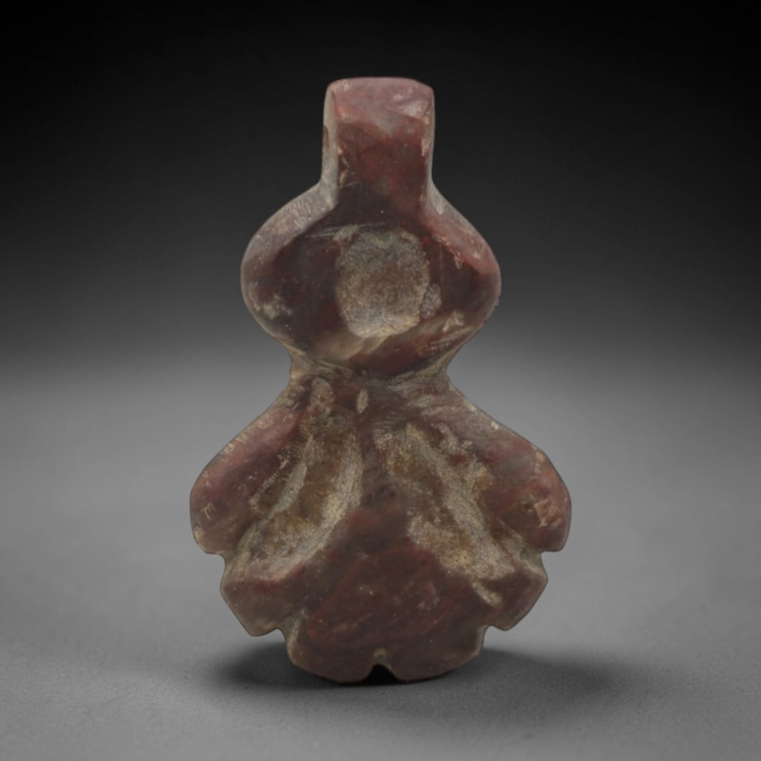 Ancient Stone Floral - Near Eastern Amulet Pendant, 42XR: Carved from reddish-brown stone, this amulet features a stylized floral form with a bulbous upper section, narrow waist, and lobed lower petals, with a pierced top for suspension. The geometric, botan