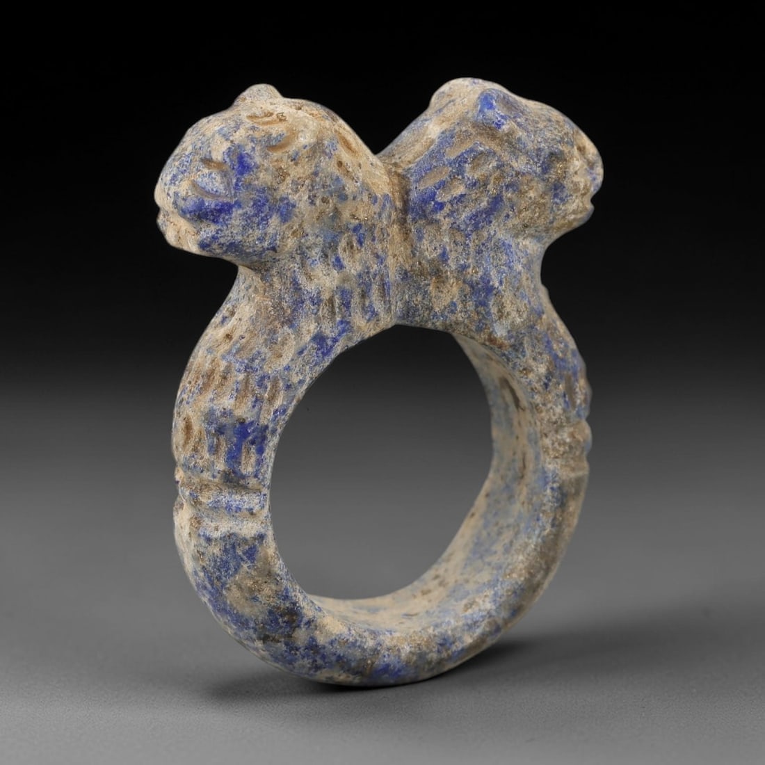 Ancient Lapis Achaemenid Ring - Zoomorphic Carving, 19AH: Carved from lapis lazuli stone, this ancient Achaemenid ring features a double-protome zoomorphic design with stylized feline heads on either side of the band, a motif characteristic of Achaemenid gly