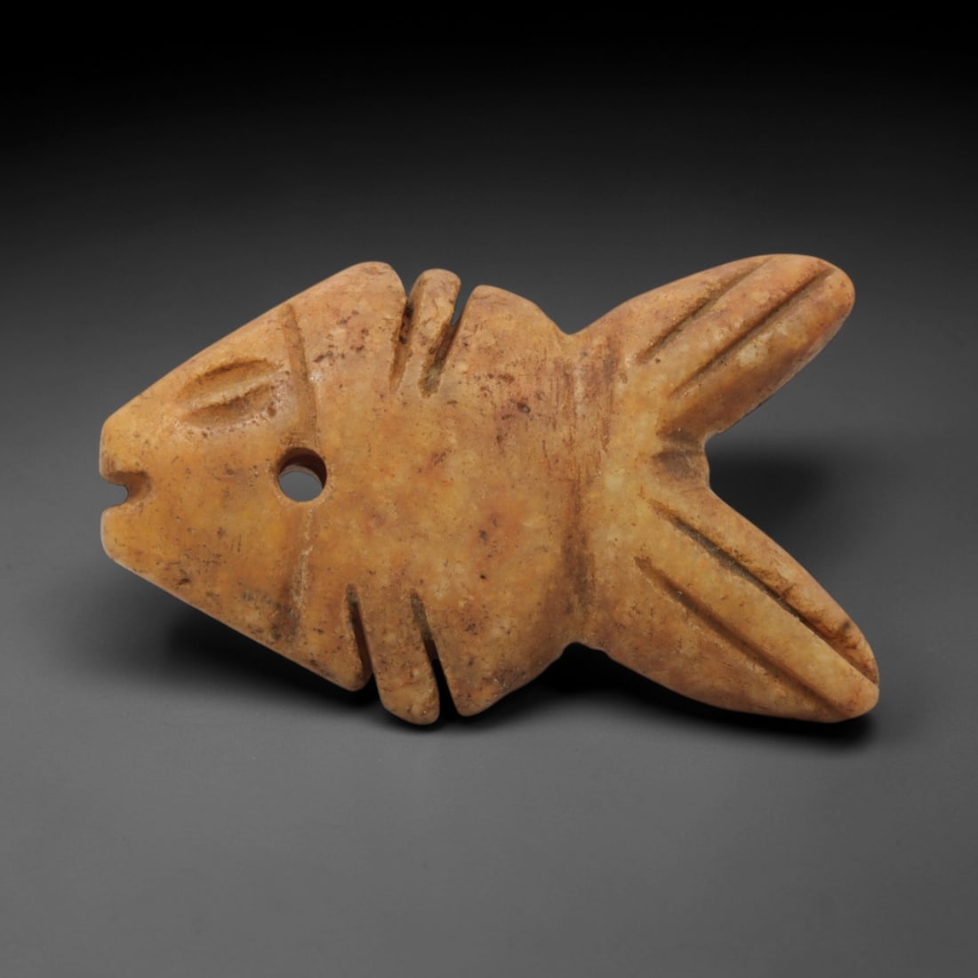 Ancient Stone Fish - Egyptian Amulet Pendant, 53XR: Carved from pale orange stone, this amulet depicts a stylized fish with incised linear details defining its fins, tail, and facial features, including a drilled suspension hole for threading as a wear