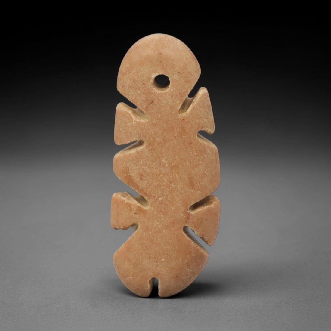 Ancient Stone Geometric Amulet - Near Eastern Pendant, 79XQ: Carved from a warm pale ochre stone, this amulet features an elongated, symmetrical form with a perforated domed top, paired angular side projections, and a notched lower edge. The repetitive geometri