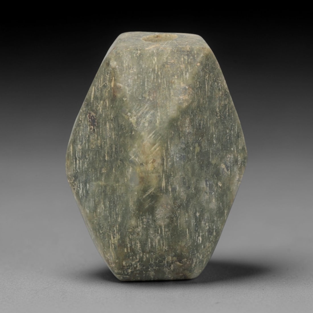 Ancient Stone Faceted Bead - Near Eastern Amulet, 58XQ: Carved from a mottled green stone, this bead takes a faceted, elongated form with a central perforation for stringing, its surface defined by multiple flat, polished planes. The geometric, multi-facet