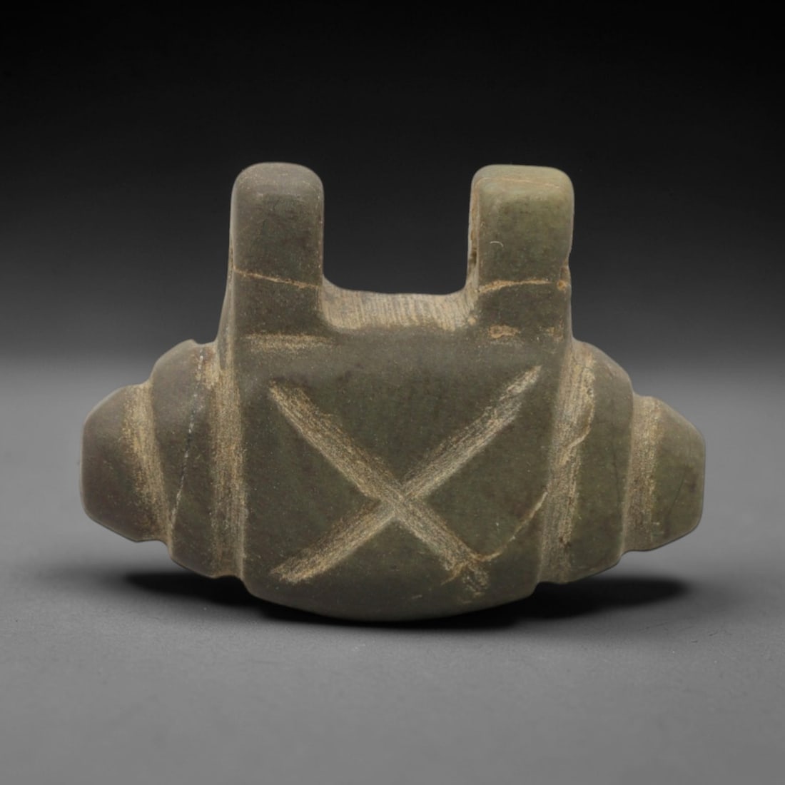 Ancient Stone Symbol Amulet - Near Eastern Ritual Figurine, 54XR: Carved from muted green stone, this amulet features a symmetrical form with two raised vertical lugs at the top, rounded lateral projections, and a central incised X-shaped symbol. The geometric desig