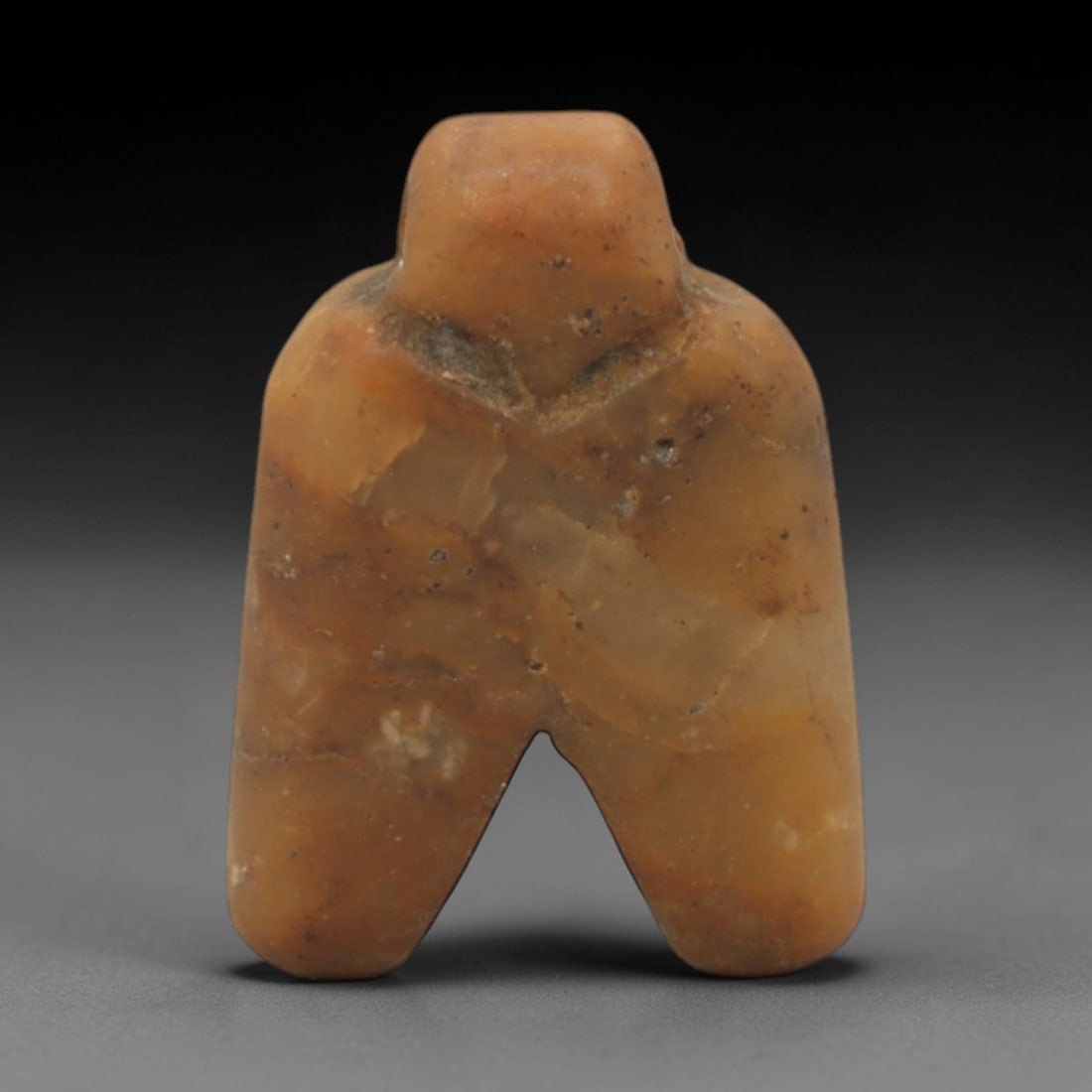 Ancient Stone Idol - Near Eastern Anthropomorphic Figurine, 41XR: Carved from warm orange-brown stone, this miniature anthropomorphic idol features a stylized form with a rounded head, broad torso, and two thick, downward-extending legs. The simplified, geometric de