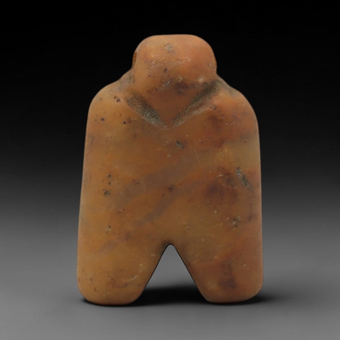 Ancient Stone Eye Idol - Near Eastern Anthropomorphic Figurine, 40XR: Carved from warm orange-brown stone, this miniature anthropomorphic idol features a stylized form with a rounded head, broad torso, and two thick, downward-extending legs. The simplified, geometric de