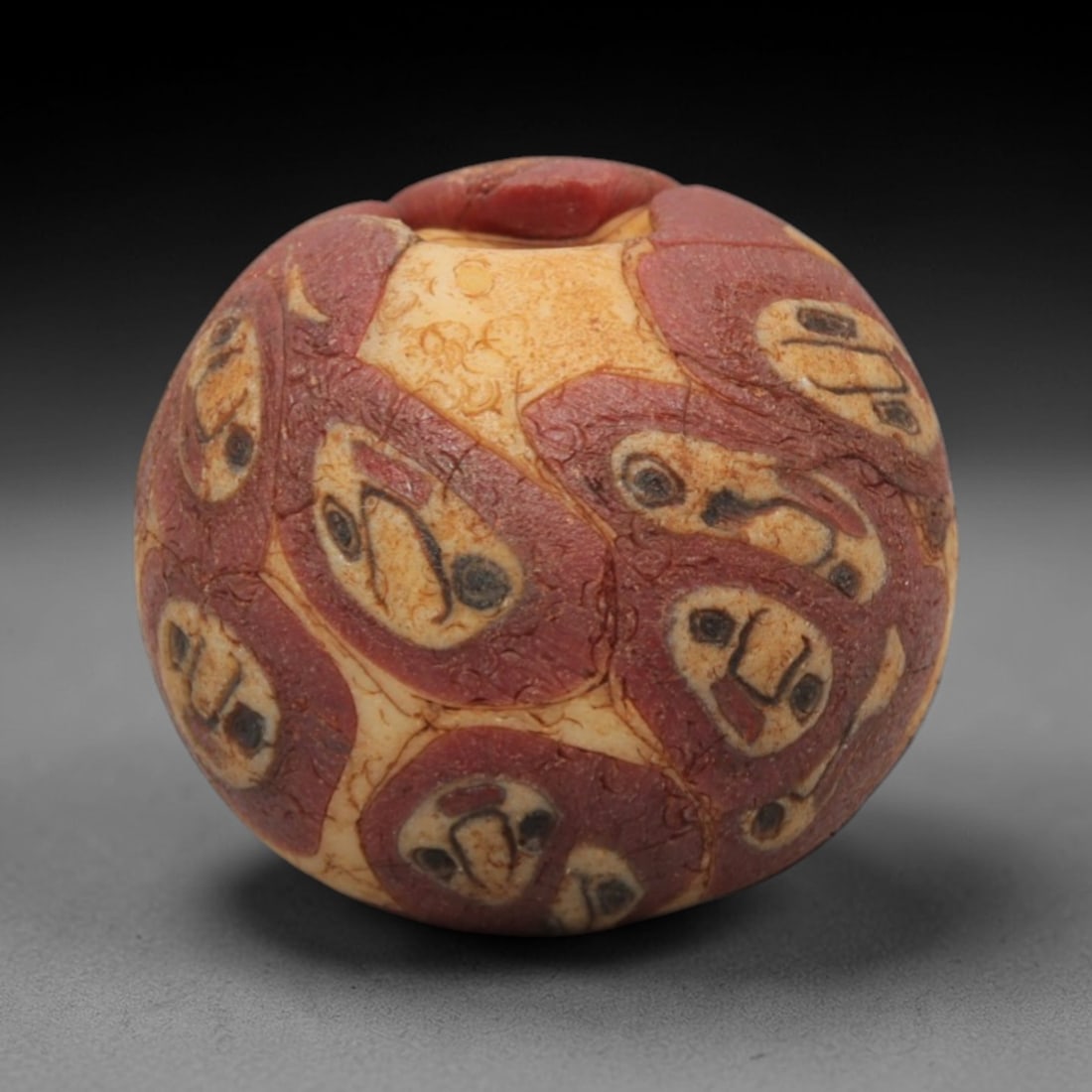 Ancient Glass Bead - Roman Egyptian Eye Amulet, 36ZN: Crafted from mosaic glass, this spherical bead features a central suspension hole and is decorated with repeating eye motifs in red, white, and black glass inlay, characteristic of Roman-Egyptian glas