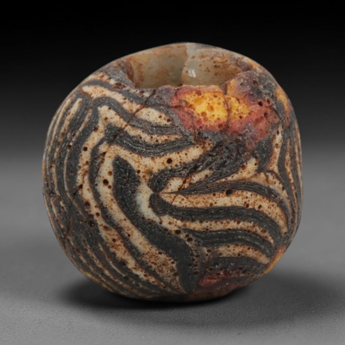 Ancient Islamic Zebra-Stripe Mosaic Glass Bead, 67ZN: A striking ancient Islamic mosaic glass bead, dating to the 8th-12th centuries CE. This spherical bead features a bold zebra-like pattern of undulating dark grey/black bands winding across a creamy wh