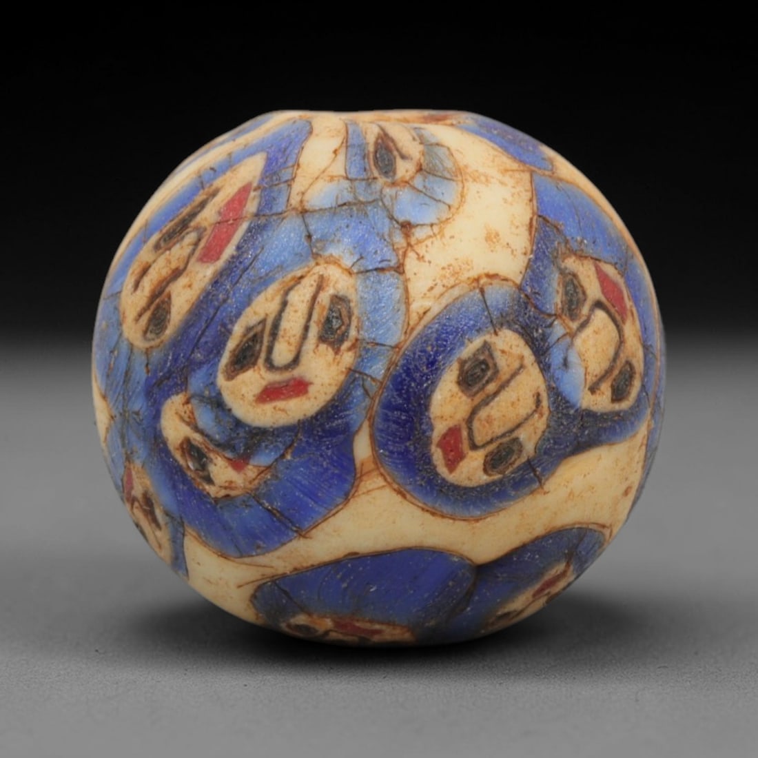 Ancient Glass Bead - Roman Egyptian Eye Amulet, 41ZN: Crafted from mosaic glass, this spherical bead features a central suspension hole and is decorated with repeating eye motifs in blue, white, red, and black glass inlay, characteristic of Roman-Egyptia