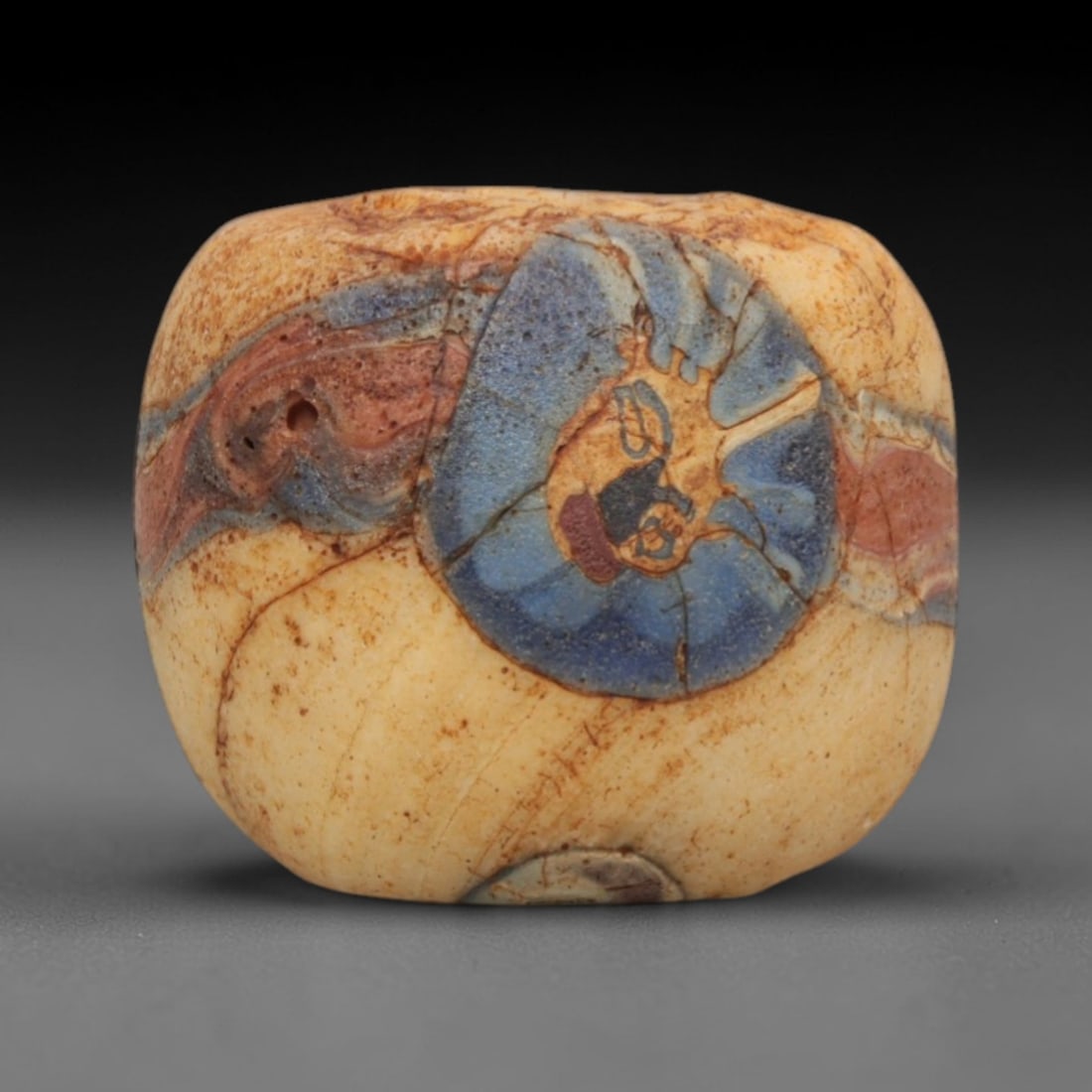 Ancient Glass Bead - Roman Egyptian Mosaic Amulet, 50ZN: Crafted from mosaic glass, this cuboid bead features a central suspension hole and is decorated with large, swirling circular motifs in blue, red, and cream glass inlay, characteristic of Roman-Egypti