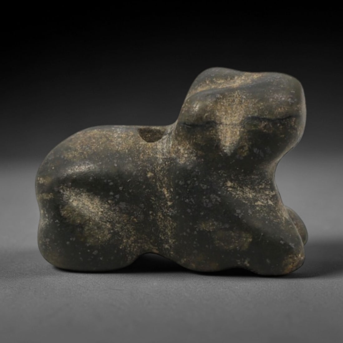 Ancient Stone Bovid - Near Eastern Amulet Figurine, 28XR: Carved from mottled dark green stone, this amulet depicts a stylized recumbent bovid with a compact, rounded body and simplified facial features. The abstract, geometric form is characteristic of Anci