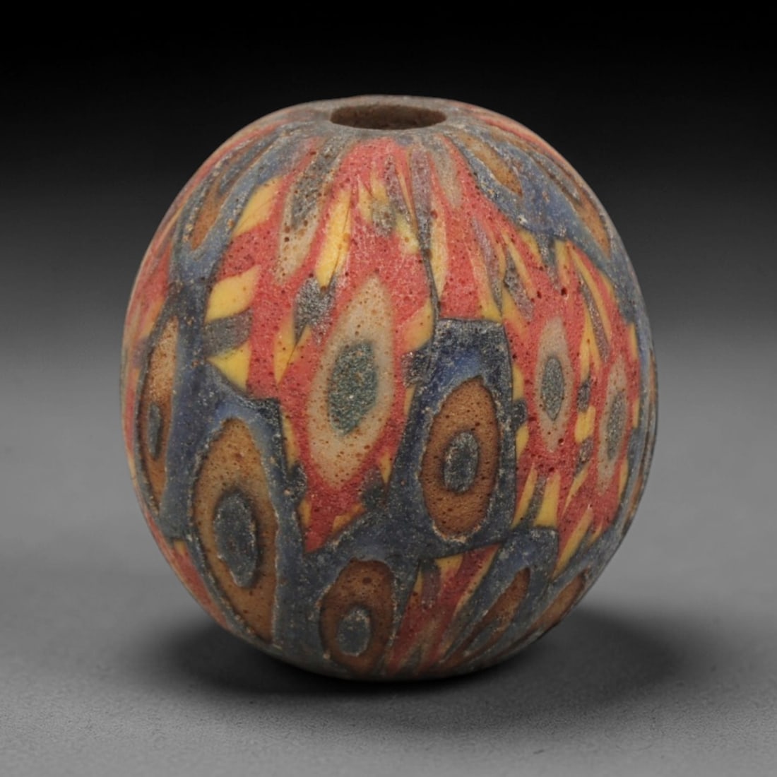 Ancient Glass Bead - Roman Egyptian Mosaic Amulet, 43ZN: Crafted from mosaic glass, this spherical bead features a central suspension hole and is decorated with intricate polychrome geometric motifs in red, yellow, blue, and brown glass inlay, characteristi