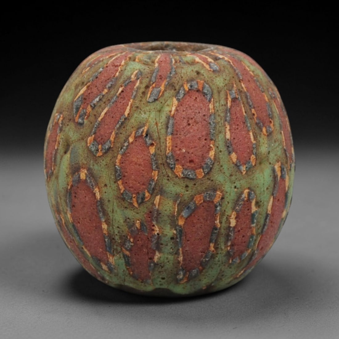Ancient Islamic Red-Green Oval Mosaic Glass Bead, 46ZN: A vibrant ancient Islamic mosaic glass bead, dating to approximately the 8th-12th centuries CE. This spherical bead features a striking geometric pattern of deep red oval panels set against a rich gre
