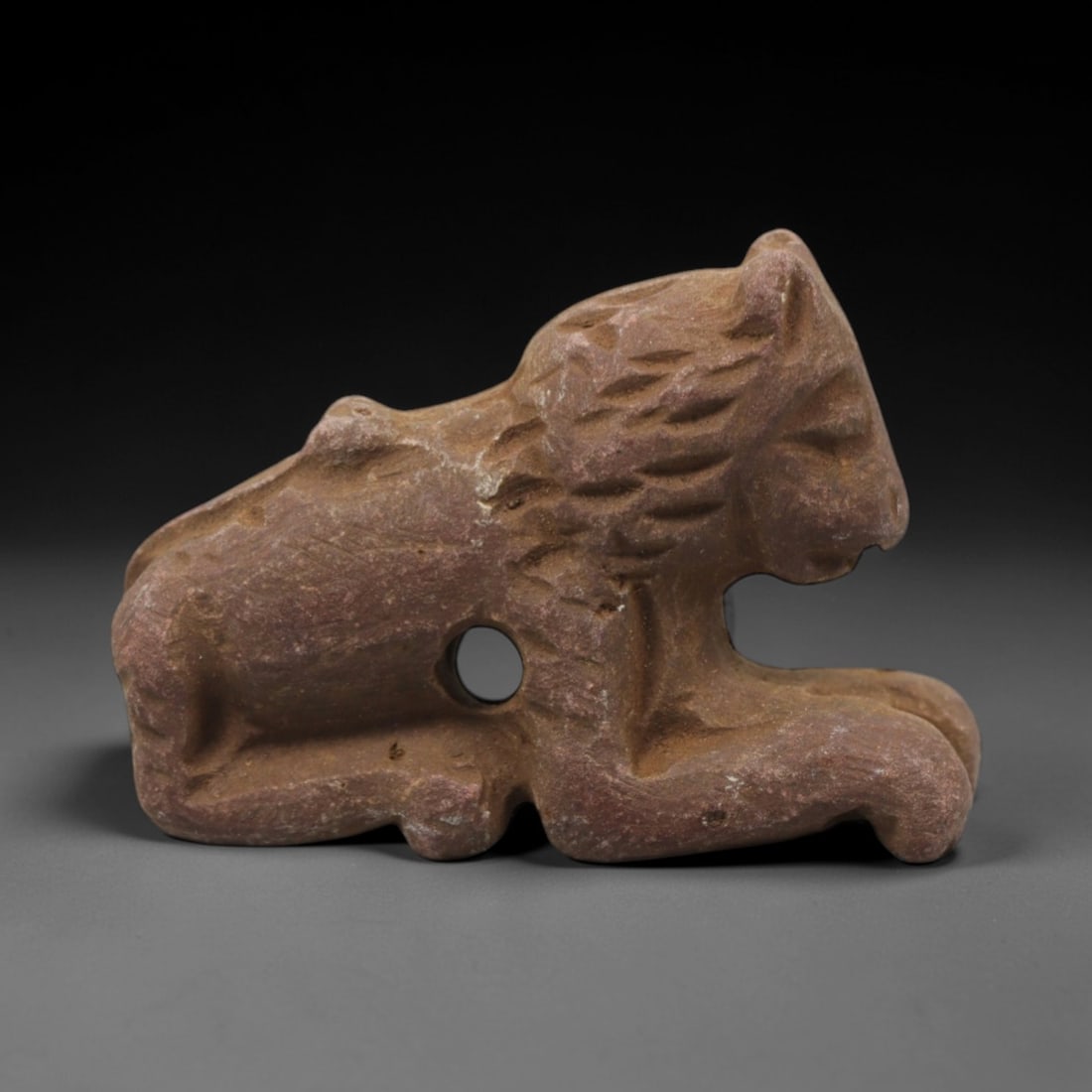 Ancient Limestone Feline Amulet - Near Eastern Figurine, 43ZQ: Carved from limestone, this small feline amulet exhibits a simplified, stylized form with incised detailing for facial features and body texture. The stone has a warm, earthy patina with minor surface