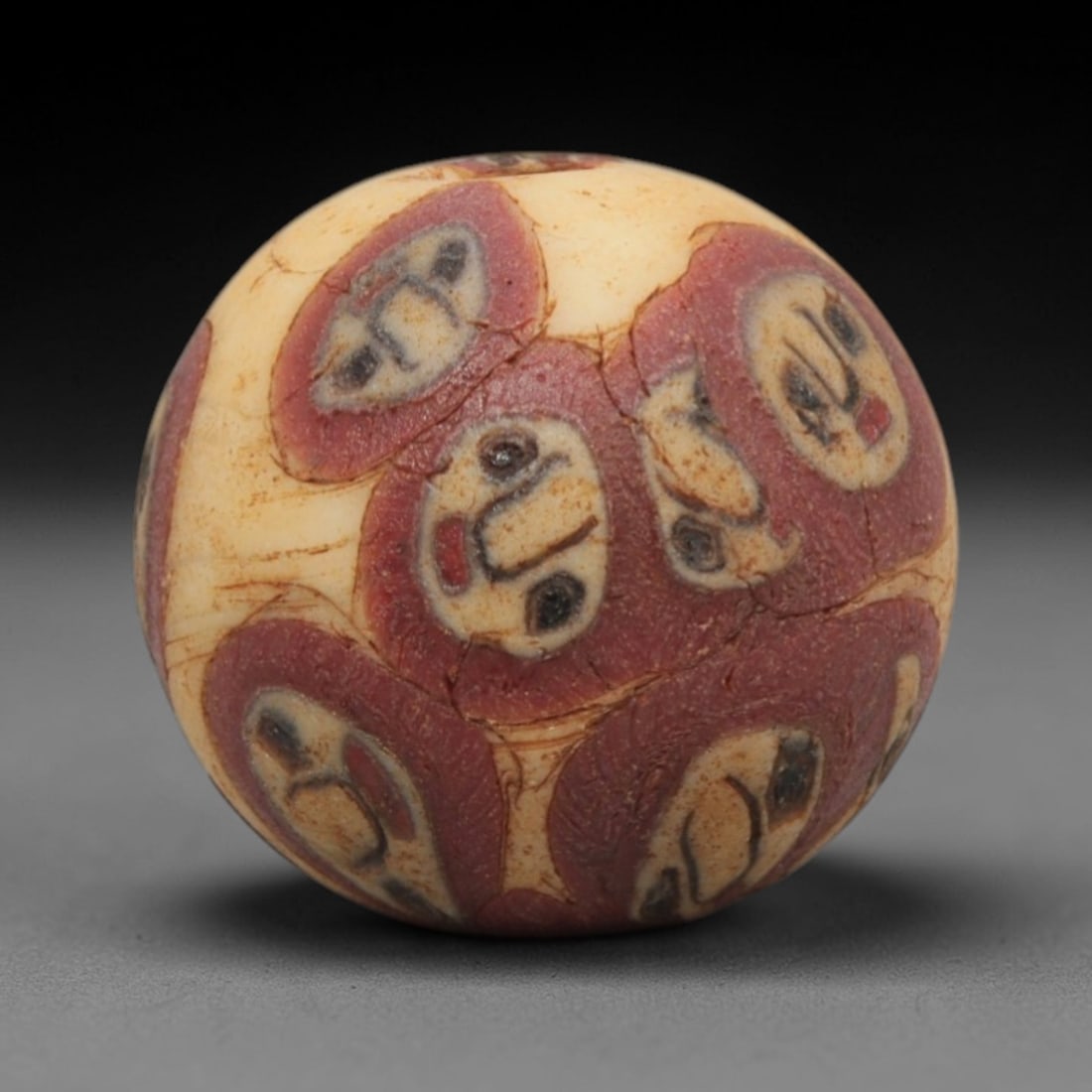 Ancient Glass Bead - Roman Egyptian Eye Amulet, 86ZN: Crafted from mosaic glass, this spherical bead features a central suspension hole and is decorated with repeating eye motifs in red, white, and black glass inlay, characteristic of Roman-Egyptian glas