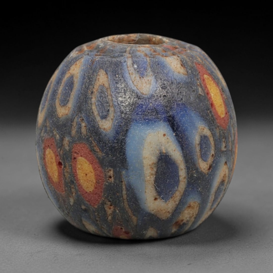 Ancient Glass Bead - Roman Egyptian Mosaic Amulet, 45ZN: Crafted from mosaic glass, this spherical bead features a central suspension hole and is decorated with repeating oval and circular motifs in blue, white, yellow, and red glass inlay, characteristic o