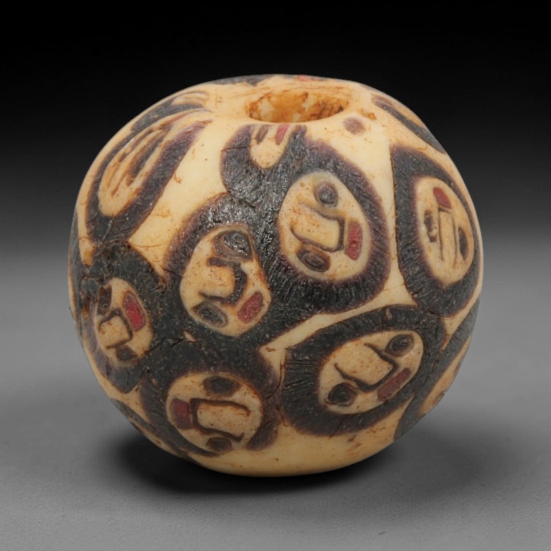 Ancient Glass Bead - Roman Egyptian Eye Amulet, 66ZN: Crafted from mosaic glass, this spherical bead features a central suspension hole and is decorated with repeating eye motifs in black, white, and red glass inlay, characteristic of Roman-Egyptian glas