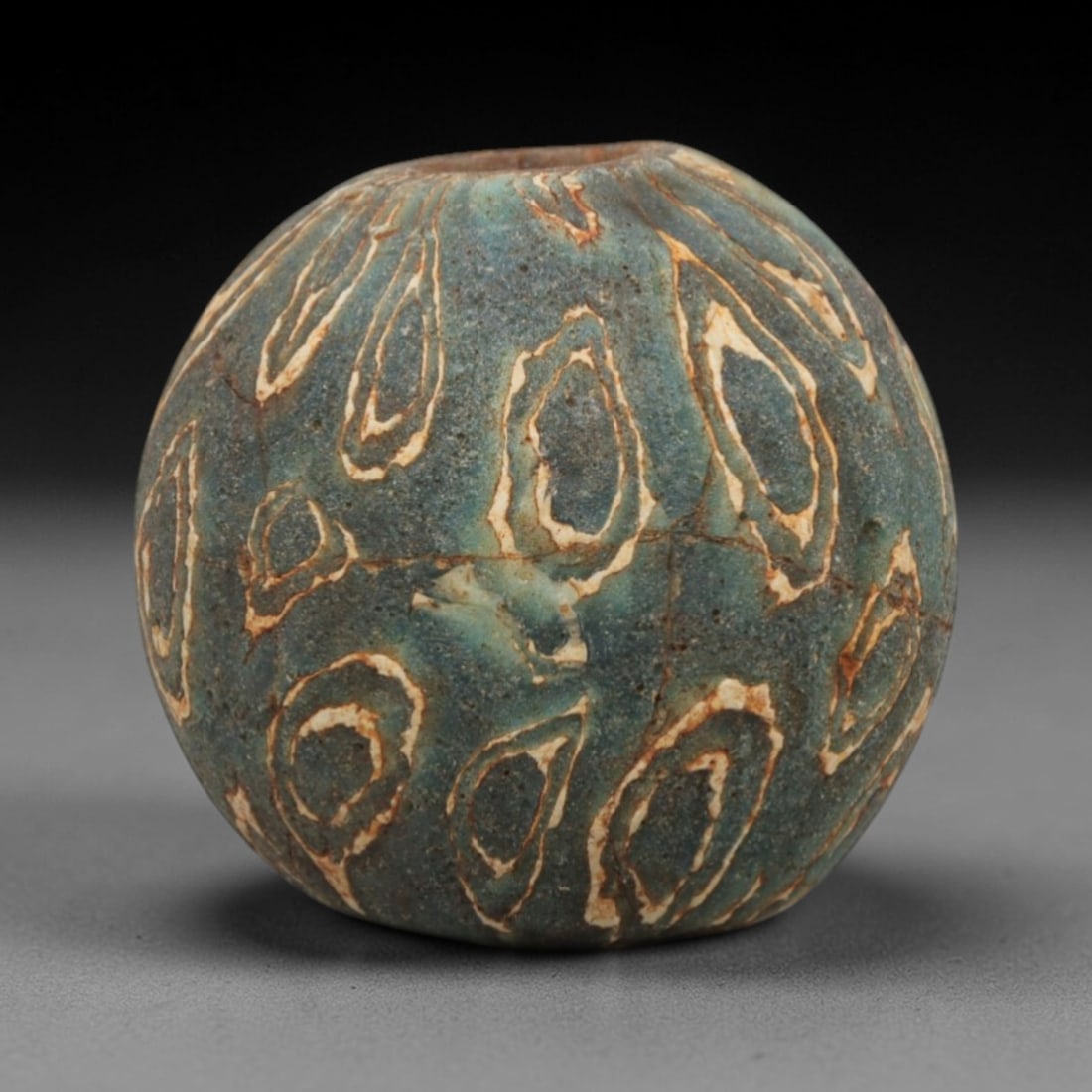 Ancient Glass Bead - Roman Egyptian Teardrop Pattern Amulet, 56ZN: Crafted from opaque glass with a distinctive teardrop-shaped concentric pattern in cream and rust-colored inlay against a teal-blue matrix, this spherical bead features a central suspension hole for w