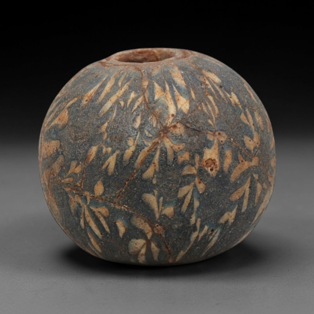 Ancient Glass Bead - Roman Egyptian Feather Pattern Amulet, 62ZN: Crafted from opaque glass with a distinctive feather-like or dendritic pattern in white and yellow against a dark blue-grey matrix, this spherical bead features a central suspension hole for wear as a