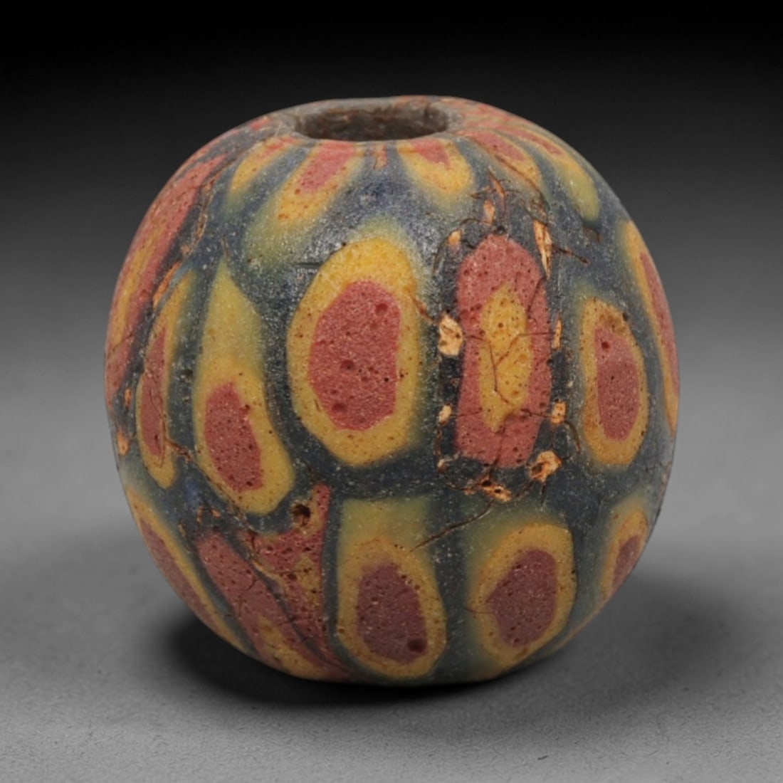 Ancient Glass Bead - Roman Egyptian Teardrop Mosaic Amulet, 39ZN: Crafted from mosaic glass, this spherical bead features a central suspension hole and is decorated with repeating teardrop-shaped motifs in red, yellow, and blue glass inlay, characteristic of Roman-E