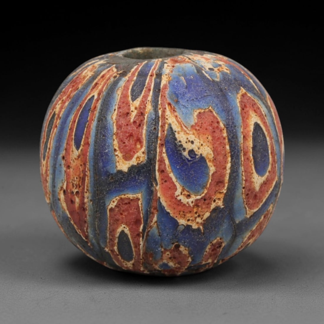 Ancient Glass Bead - Roman Egyptian Mosaic Amulet, 42ZN: Crafted from mosaic glass, this spherical bead features a central suspension hole and is decorated with bold, abstract geometric motifs in red, blue, and white glass inlay, characteristic of Roman-Egy