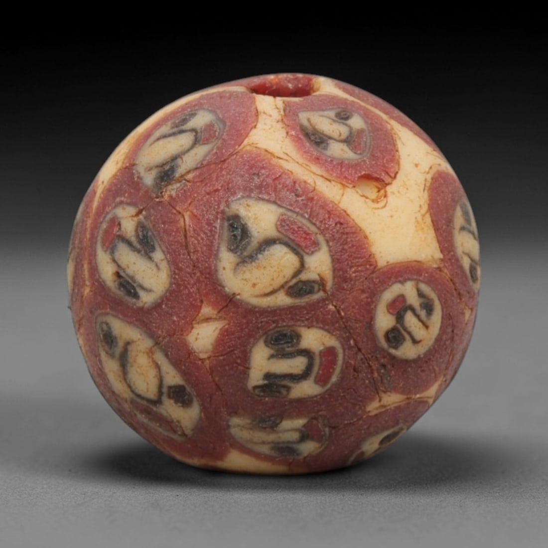 Ancient Glass Bead - Roman Egyptian Mosaic Amulet, 44ZN: Crafted from mosaic glass, this spherical bead features a central suspension hole and is decorated with repeating stylized motifs in red, white, and black glass inlay, characteristic of Roman-Egyptian