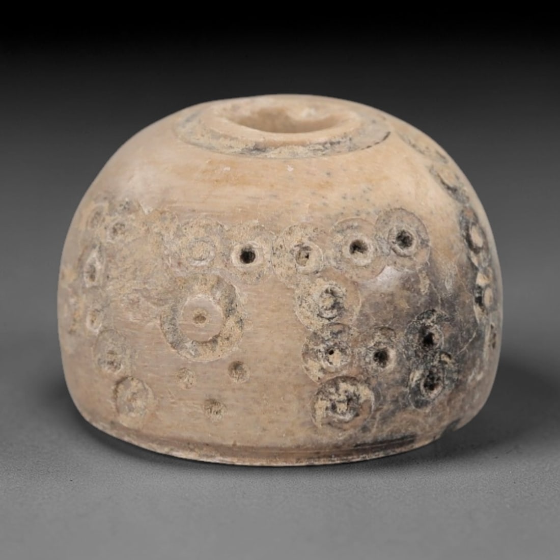 Ancient Bone Spindle Whorl - Near Eastern Dot-in-Circle Motif, 68XR: This ancient Near Eastern spindle whorl is crafted from bone, featuring incised dot-in-circle motifs surrounding the central perforation. The compact, rounded form is a traditional textile tool used t