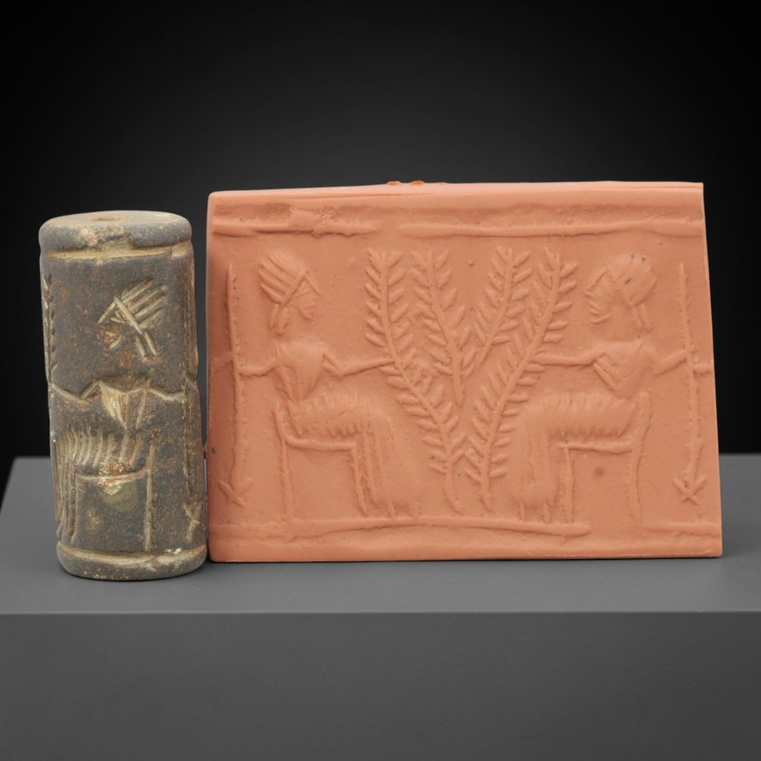 Ancient Terracotta Cylinder Seal - Near Eastern Glyptic Art, 78ZQ: Carved from terracotta, this ancient Near Eastern cylinder seal features an intaglio scene depicting seated figures flanked by vegetal motifs, a common compositional type in Mesopotamian glyptic art.