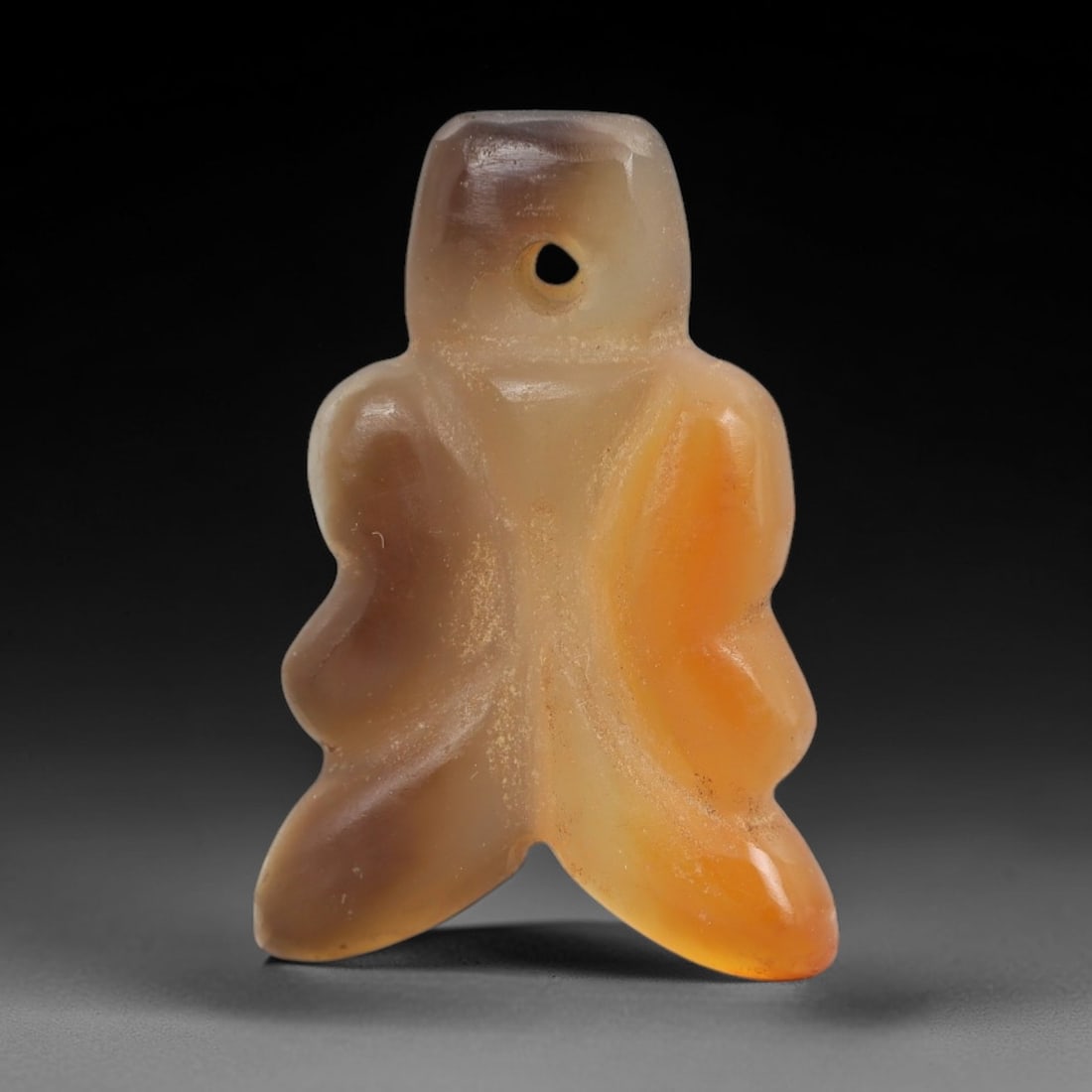 Ancient Agate Anthropomorphic Amulet - Near Eastern Figurine, 38AJ: Carved from banded orange-and-brown agate, this amulet is formed as a stylized anthropomorphic figure with a rounded head, simplified torso, and two curved lower projections, consistent with ancient N