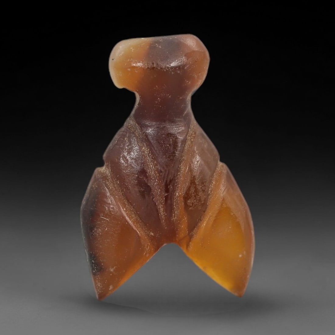 Ancient Agate Bird Amulet - Near Eastern Figurine, 48AJ: Carved from banded brown-and-orange agate, this amulet is formed as a stylized bird with a rounded head, narrow neck, and pointed wing-like lower projections, featuring incised linear detailing across