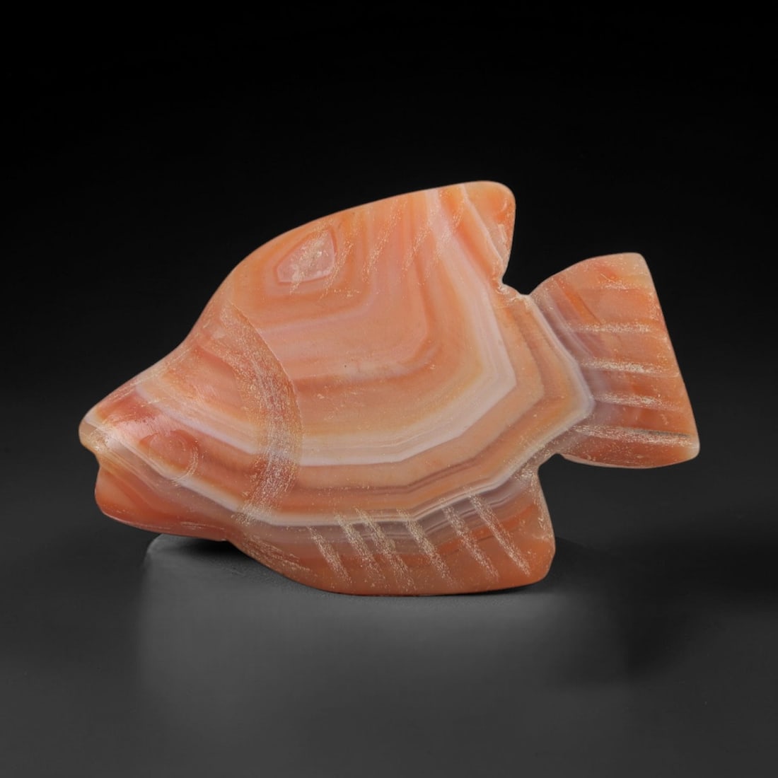 Ancient Banded Agate Fish Amulet - Egyptian Figurine, 27AJ: Carved from striking banded agate with alternating orange and white concentric layers, this amulet is formed as a stylized fish with incised linear detailing across the fins and tail to denote feather