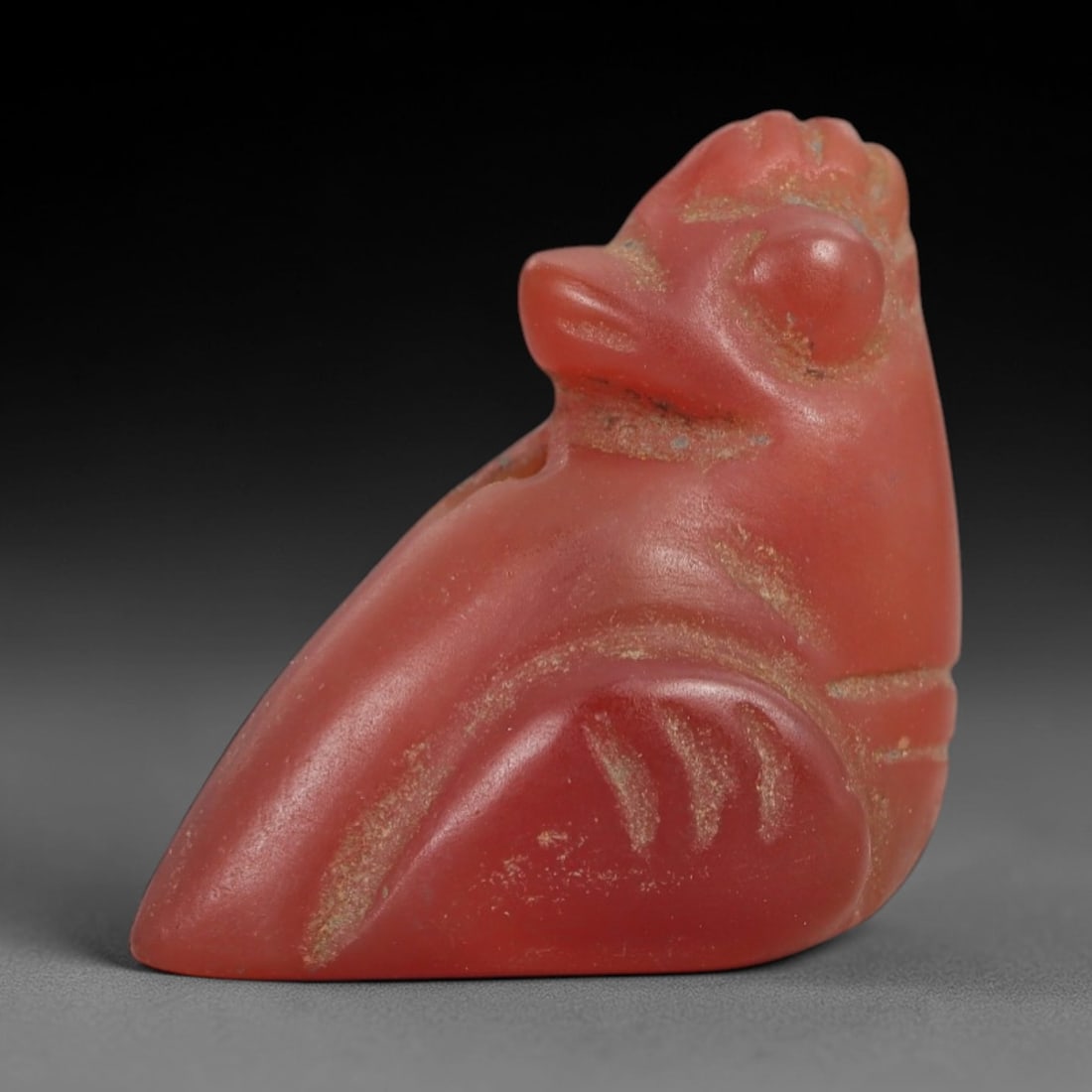 Ancient Carnelian Bird Amulet - Egyptian Figurine, 34AJ: Carved from vibrant red carnelian, this amulet is formed as a stylized bird with a crested head, rounded eye, and distinct beak, featuring incised linear detailing across the body to denote feather pa