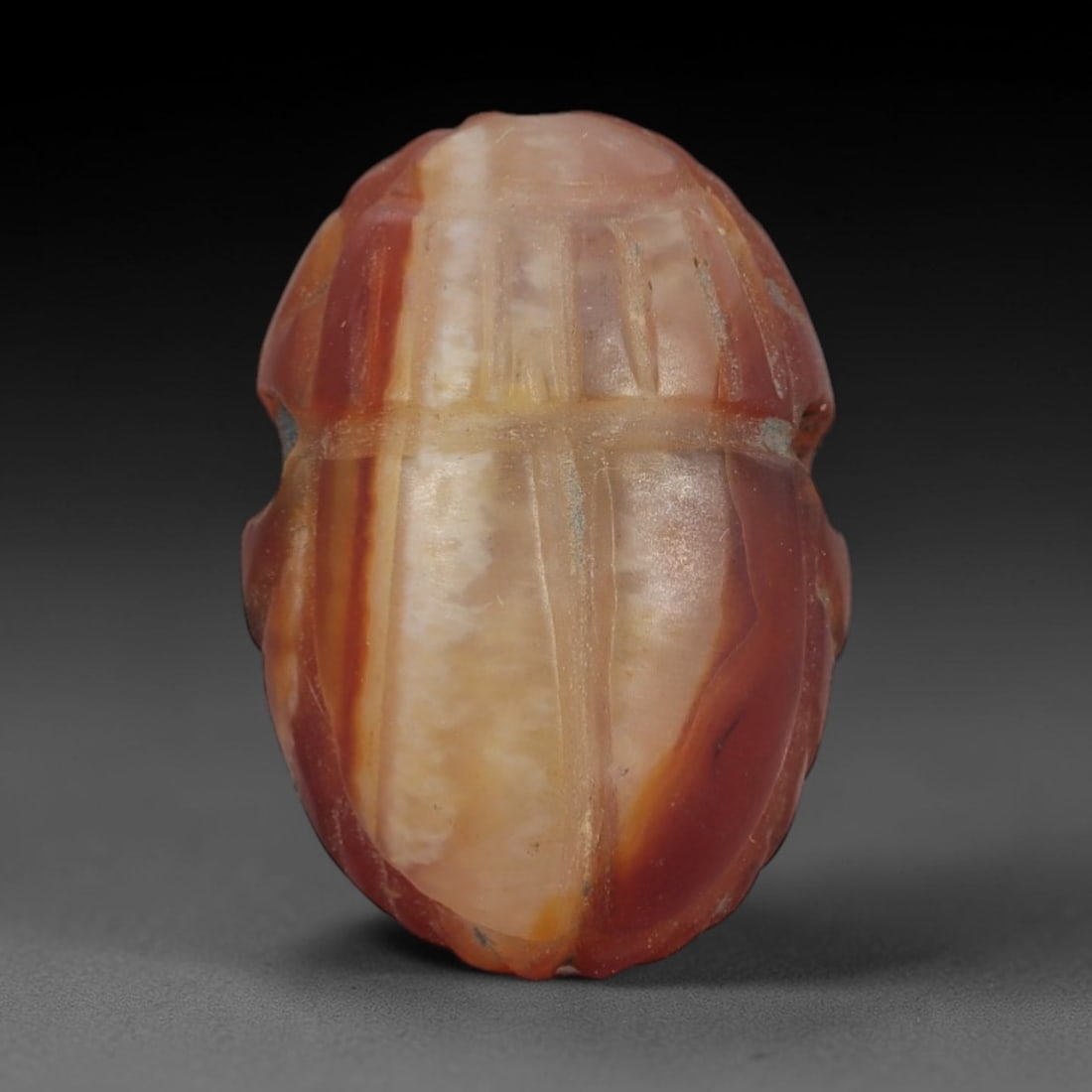 Ancient Banded Agate Scarab Amulet - Egyptian Figurine, 55AJ: Carved from striking banded agate with creamy white and warm orange-red vertical layers, this amulet is formed as a stylized scarab beetle with incised linear detailing to define segmented wing cases