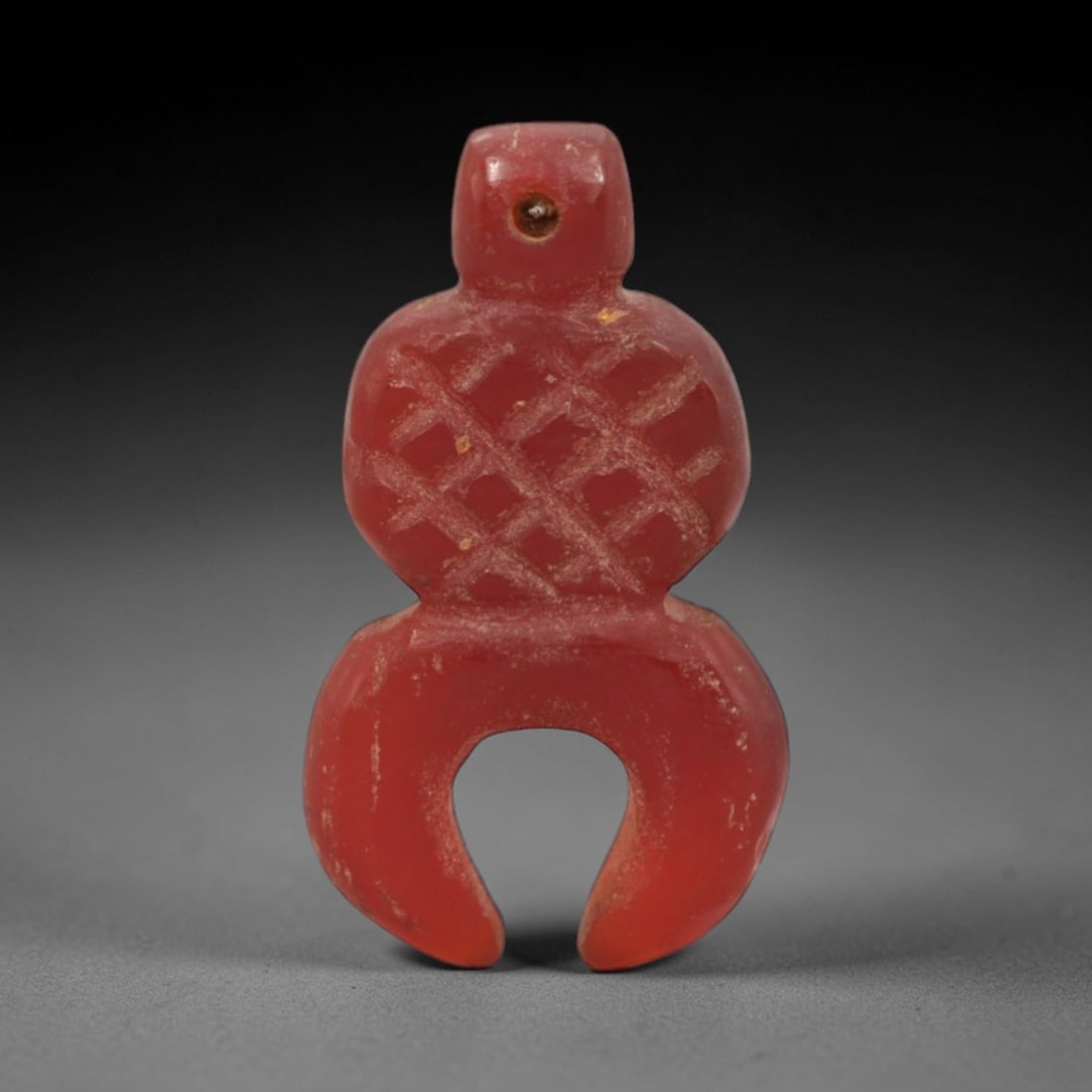 Ancient Carnelian Knot - Egyptian Amulet Figurine, 95XS: Carved from rich, opaque carnelian with natural surface patination and minor wear, this amulet takes the form of a stylized knot with a U-shaped lower terminal, featuring incised crisscross detailing