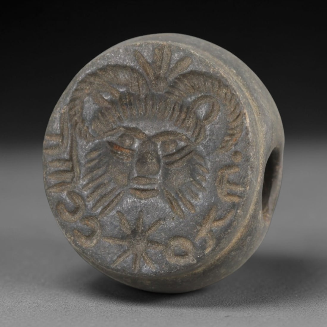Ancient Sasanian Steatite Hemispherical Stamp Seal - Anthropomorphic, 54AK: Carved from steatite, this hemispherical Sasanian stamp seal features a central anthropomorphic face motif with stylized facial features, horned headdress, and surrounding epigraphic script alongside