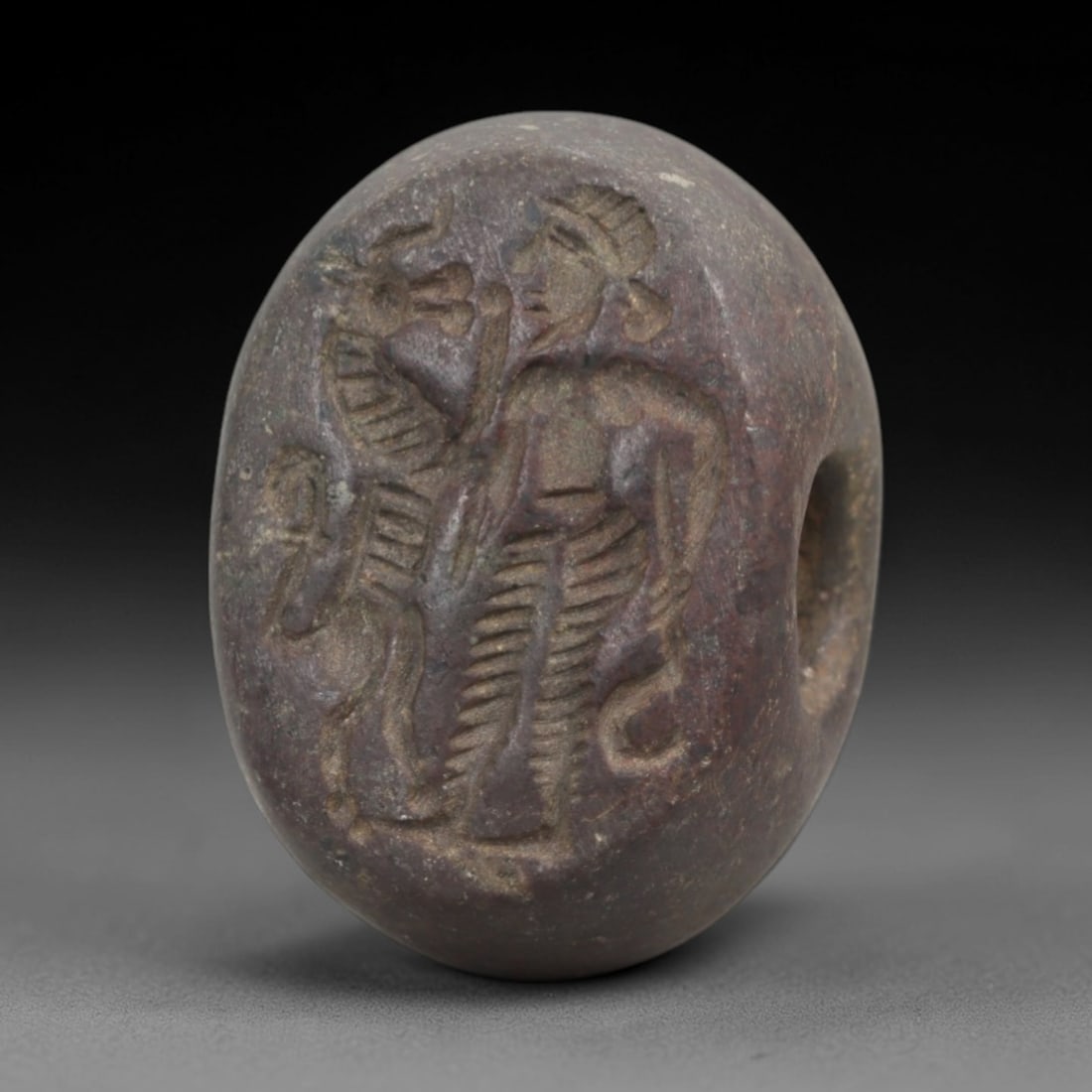 Ancient Steatite Stamp Seal - Sasanian Warrior and Feline, 47AK: Carved from steatite, this hemispherical Sasanian stamp seal features a central composition of a standing warrior alongside a stylized feline, with incised details defining the warrior's attire, postu