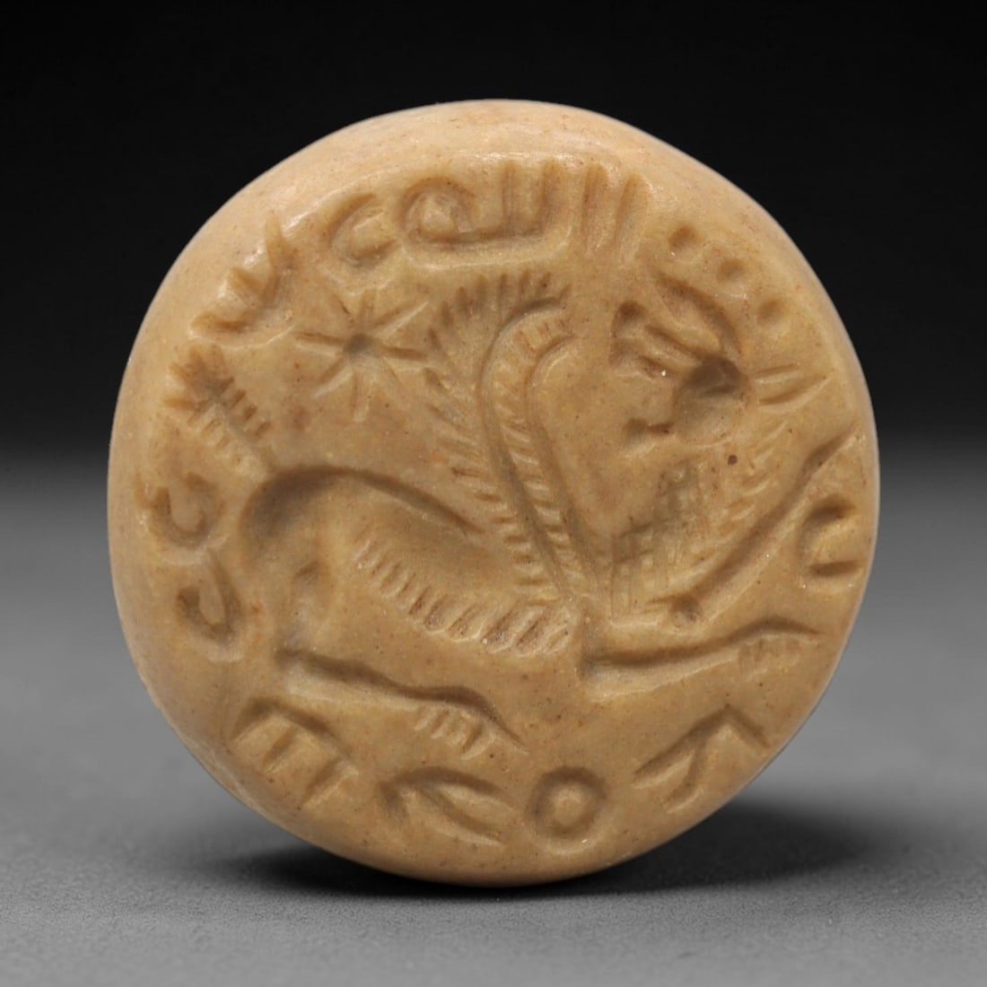 Ancient Steatite Hemispherical Stamp Seal - Near Eastern, 26XV: Carved from steatite, this hemispherical stamp seal features a circular impression depicting a winged anthropomorphic figure alongside a star motif, with surrounding script consistent with ancient Nea