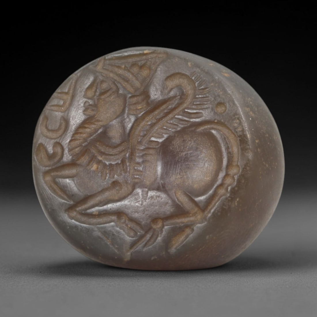 Ancient Steatite Stamp Seal - Sasanian Lamassu, 50AK: Carved from steatite, this hemispherical Sasanian stamp seal features a central lamassu motif-a winged, anthropomorphic hybrid figure with a bearded human face, avian wings, and quadrupedal body-with