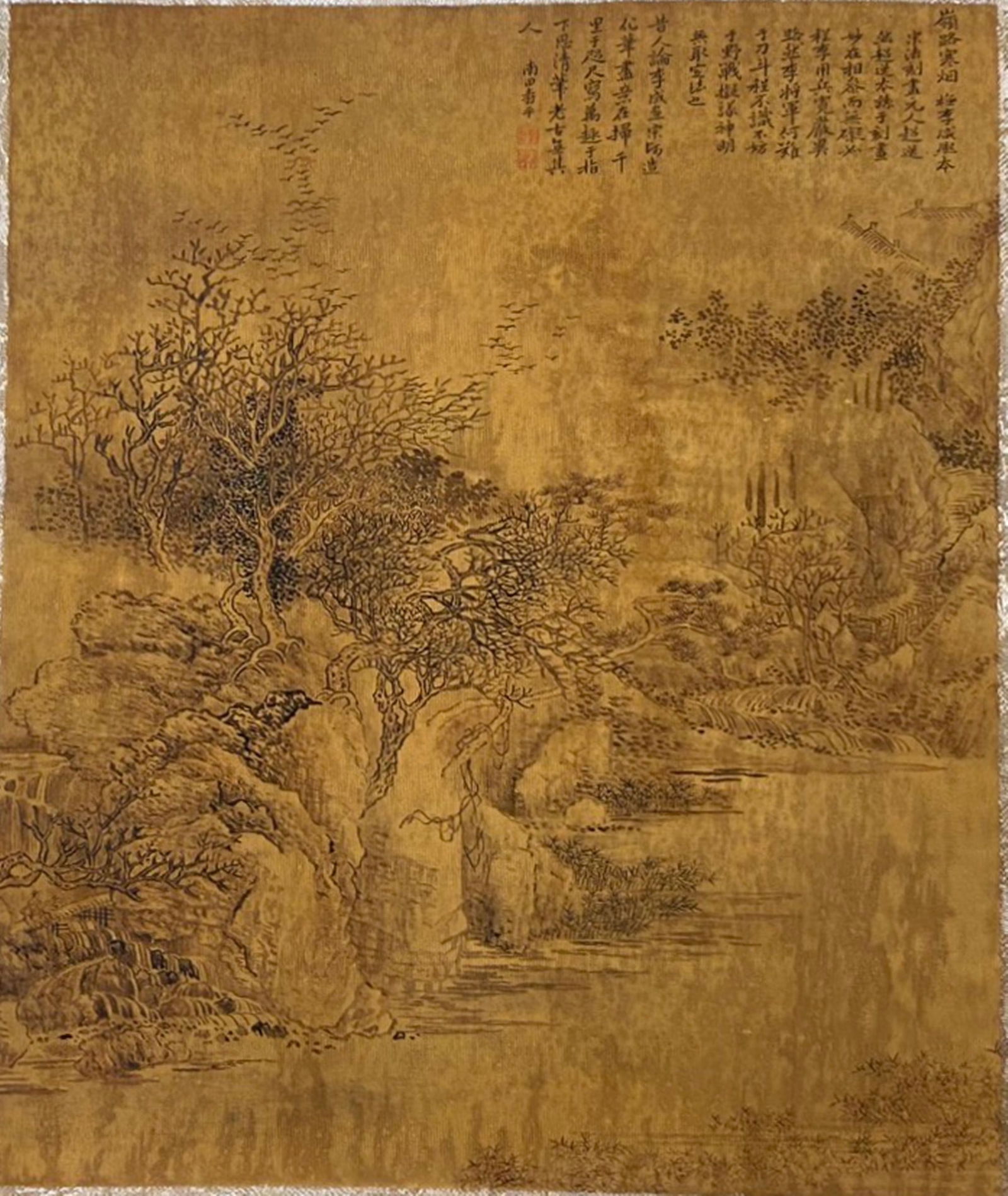 A Chinese Ink and Color Textile Print, Cold Forest and Misty River, 20th Century, 26FK: Printed on woven silk or hemp textile with a gold-toned ground, the composition depicts a sparse winter landscape. Bare, gnarled trees cling to rocky outcrops beside a calm river, with flocks of birds