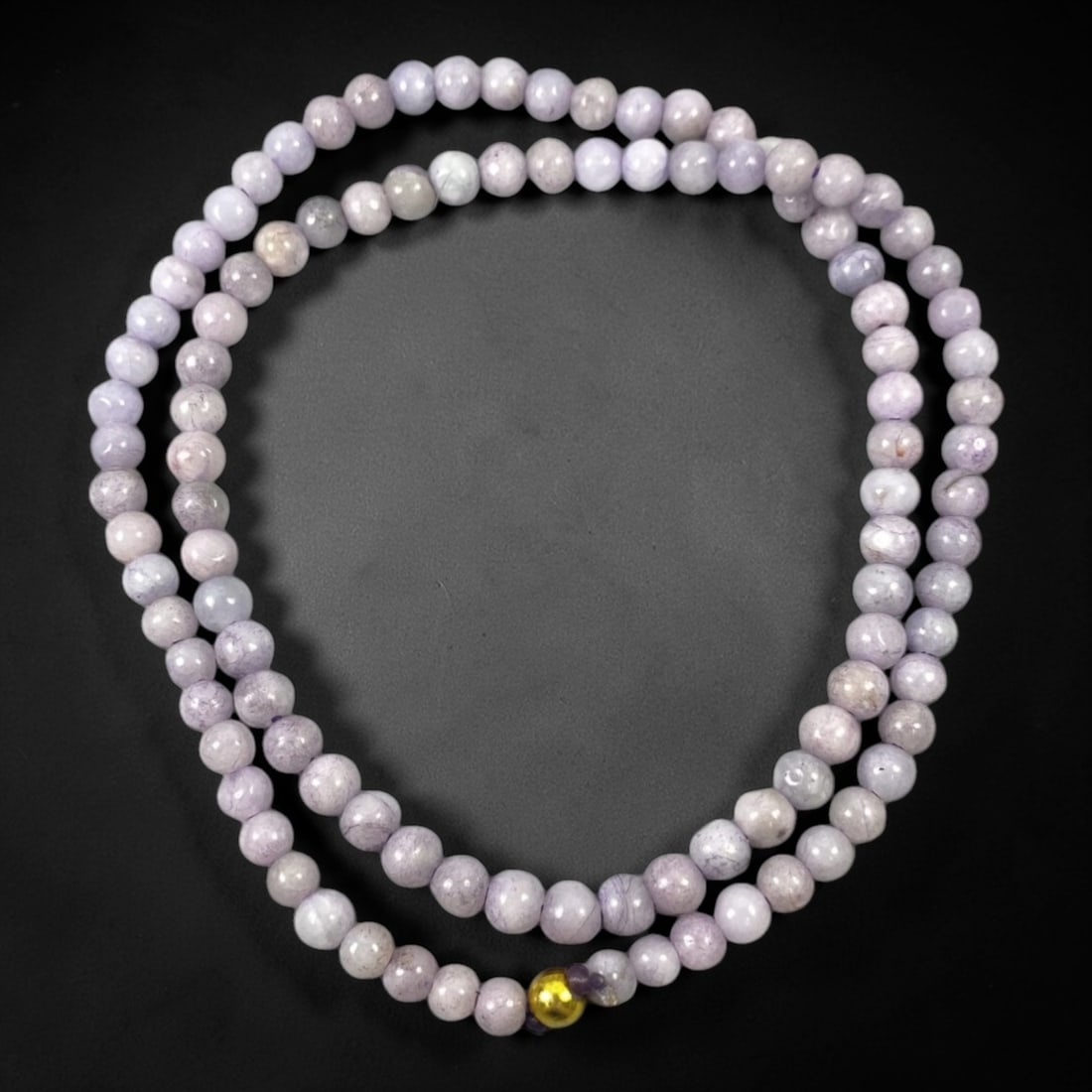 A Chinese Jadeite Jade Bead Necklace, 20th Century, 70ZK: Composed of spherical beads of pale lavender and white jadeite jade with natural veining and subtle tonal variations, the necklace is strung in a continuous loop. The beads exhibit a smooth, polished