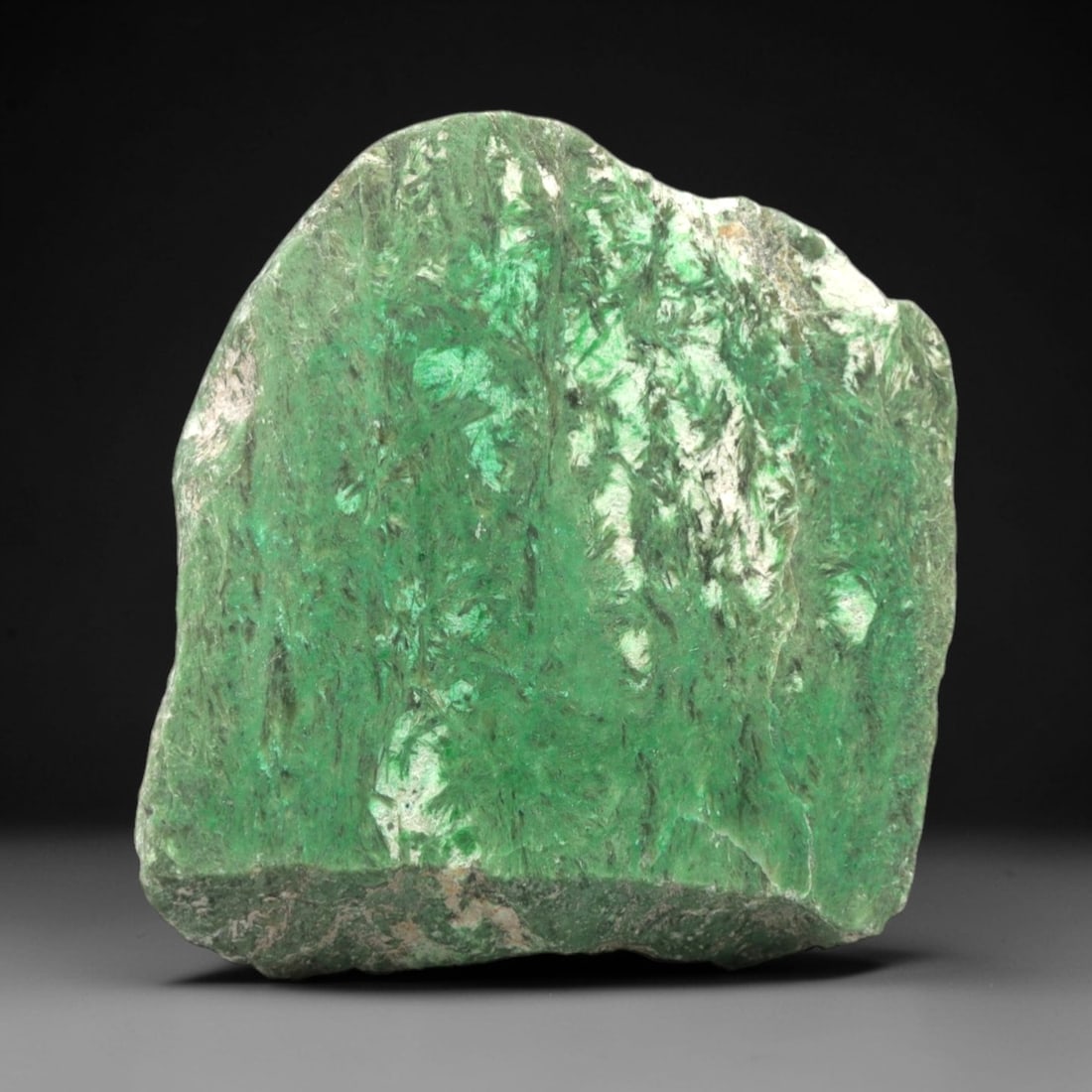A Burmese Jadeite Jade Rough, 20th Century, 55FS: A piece of Burmese jadeite jade rough, with a vibrant green matrix and prominent white mineral inclusions. The rough is shaped as an irregular, angular form, with visible natural fractures and a parti