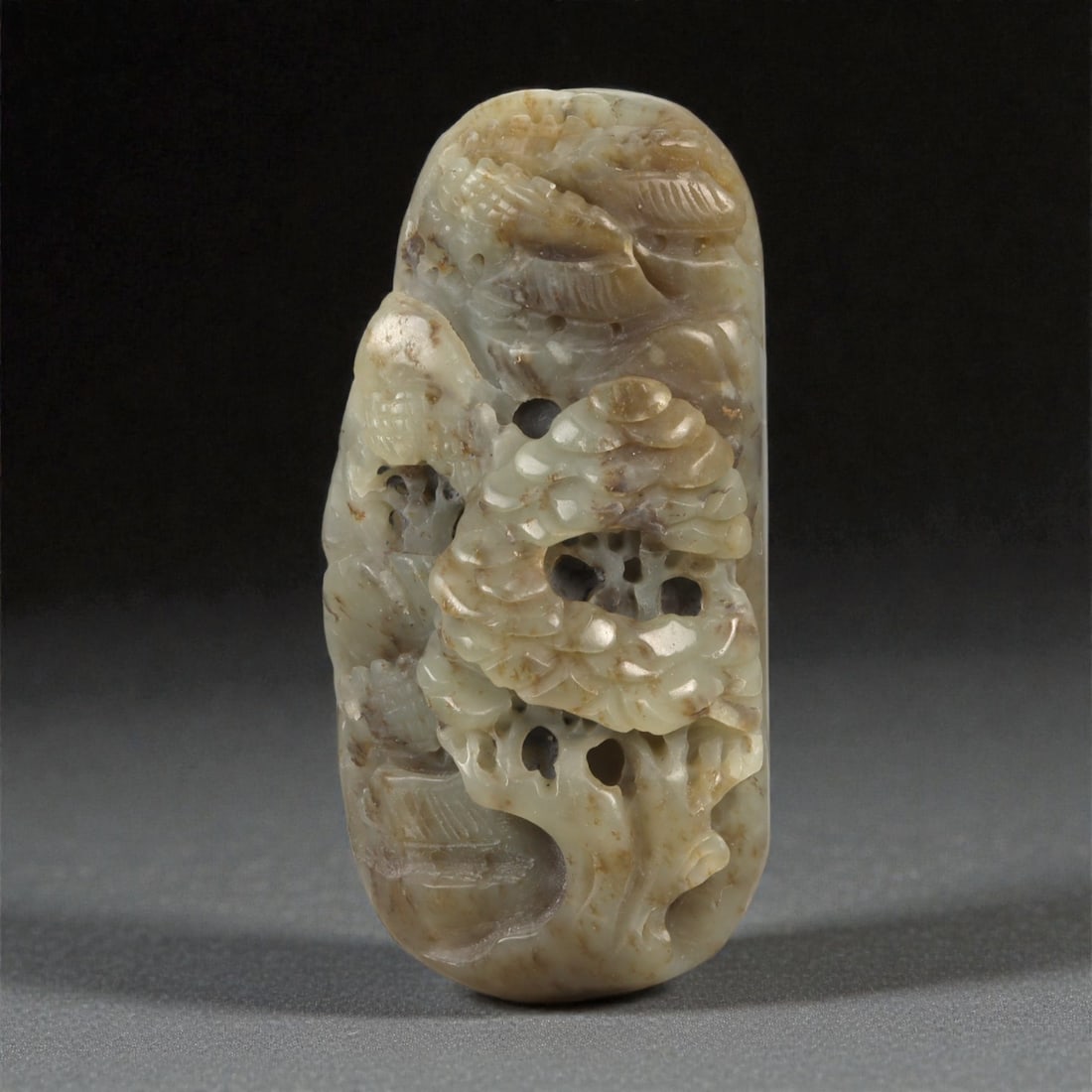 A Chinese Jade Openwork Rockwork Pendant, 20th Century, 27YA: Carved from pale celadon jade with extensive russet and honey-colored inclusions, the pendant is of elongated rectangular form with rounded ends, worked in high relief and pierced openwork. The design