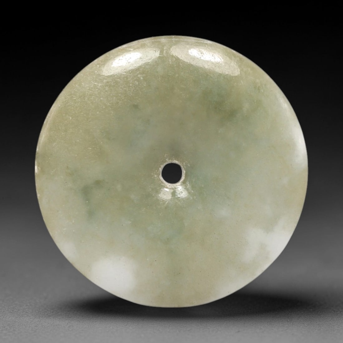 A Chinese Jadeite Jade Bi Disc, 20th Century, 47FR: Carved from solid celadon jadeite jade with uniform coloration and subtle granular internal texture, the object is formed as a circular bi disc with a centrally drilled aperture. The surface is polish