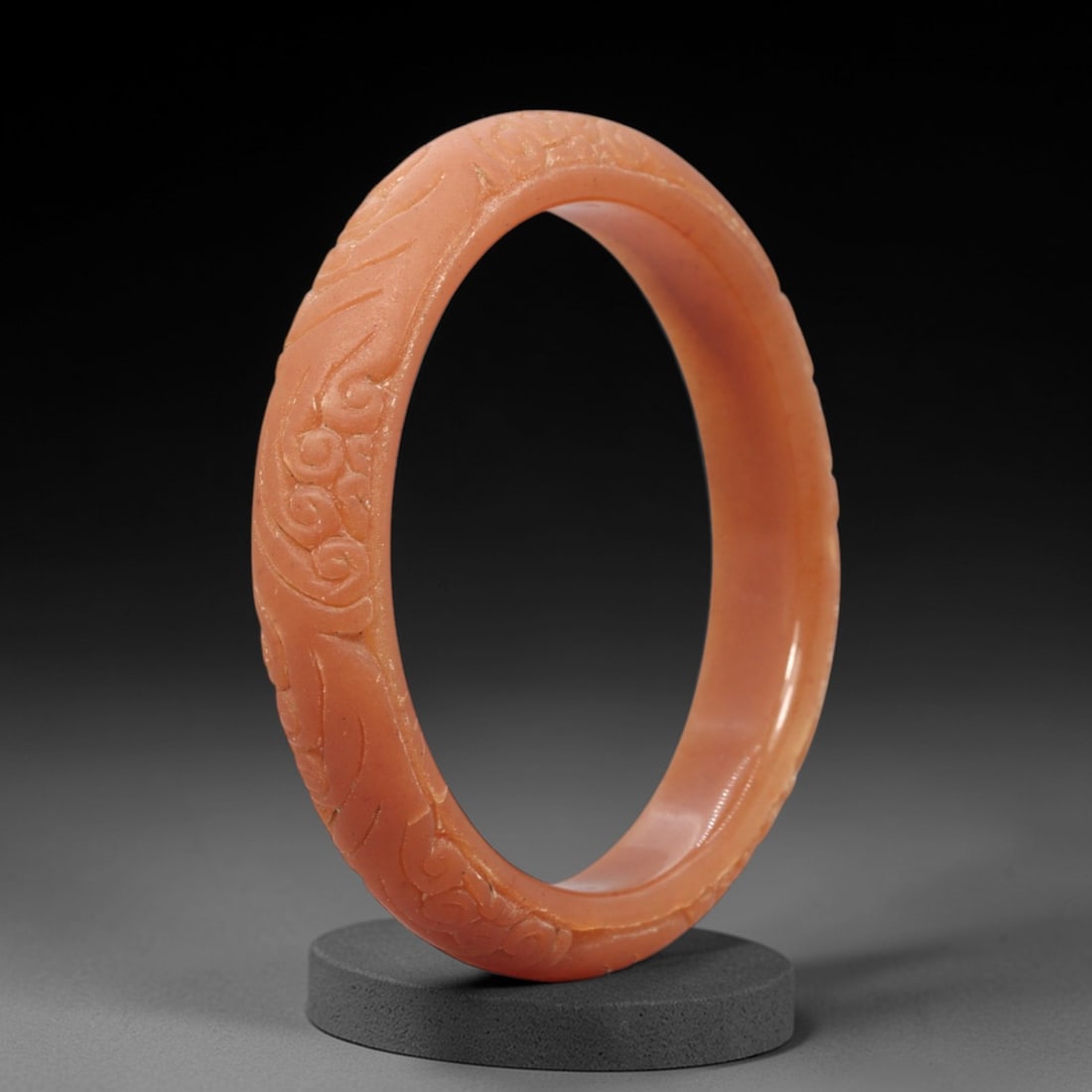 A Chinese Jadeite Jade Bangle Bracelet, 20th Century, 45FS: Carved from warm, peach-toned jadeite jade with a smooth, polished finish, the bangle is formed as a continuous circular band. The exterior surface is decorated with continuous relief carving depictin