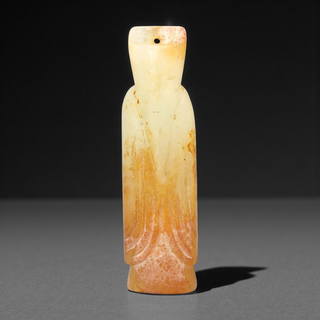 A Chinese Archaistic-Style Hetian Jade Amulet Figure, 20th Century, 56FH: Carved from pale creamy-white Hetian jade with areas of russet and honey-colored staining, the object is formed as a slender standing figure with an elongated body and simplified proportions. The head